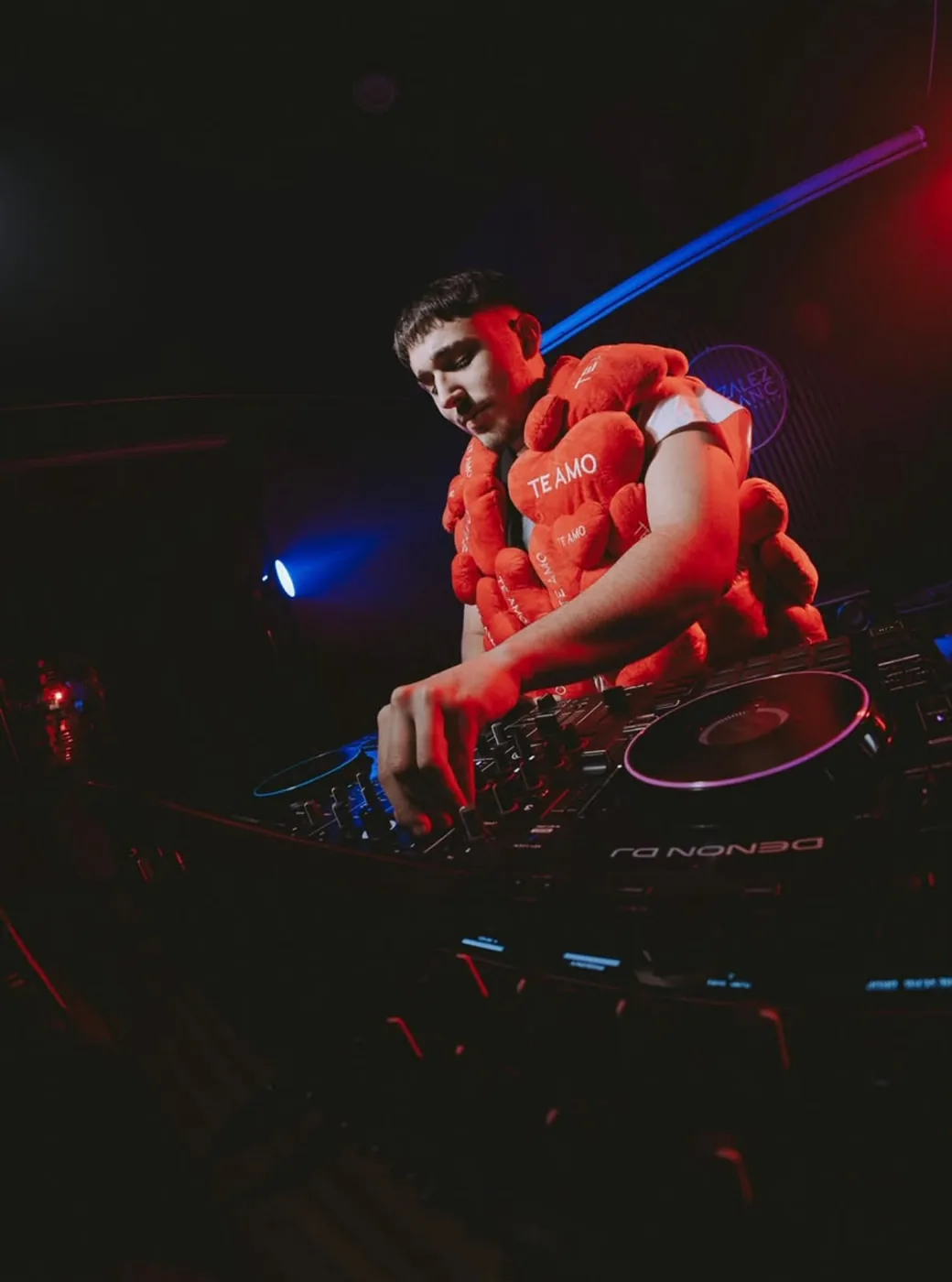 DJVALENOK mezclando en los decks, tomado desde abajo, con luces rojas y azules