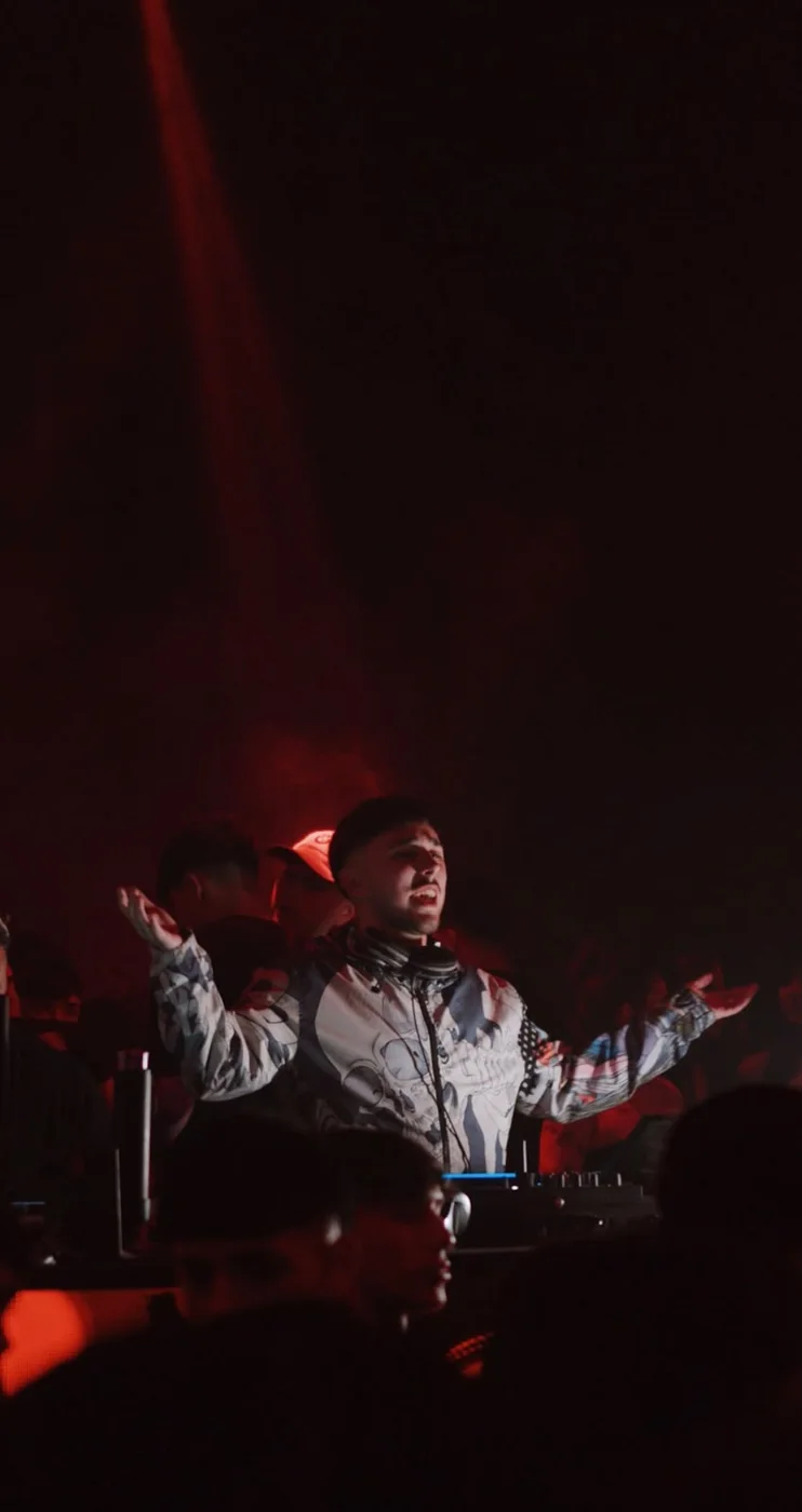 DJVALENOK con los brazos abiertos frente al público, bajo luz roja, en Pika
