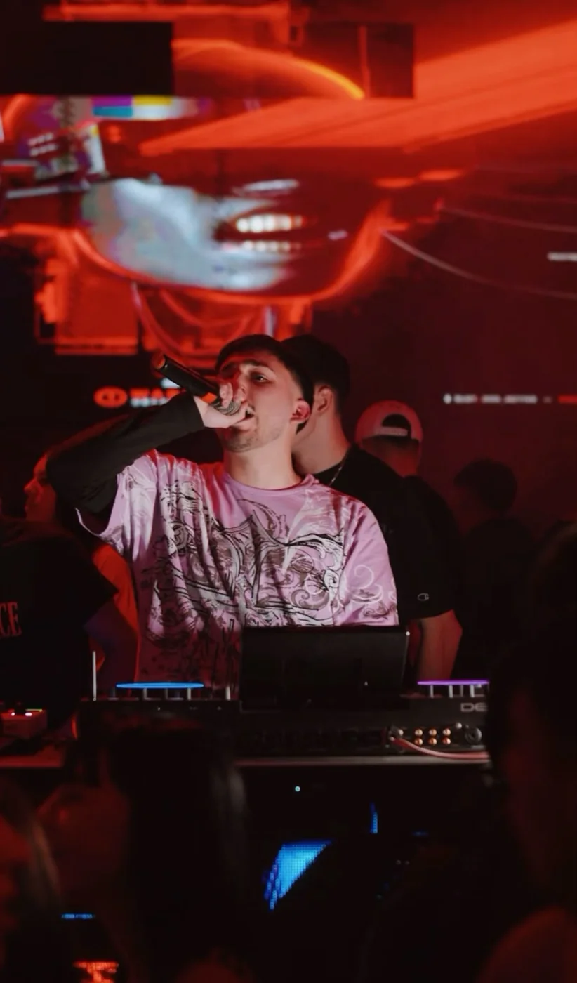 DJVALENOK con el micrófono frente al público, bajo luz roja, en una fecha en Noche Real